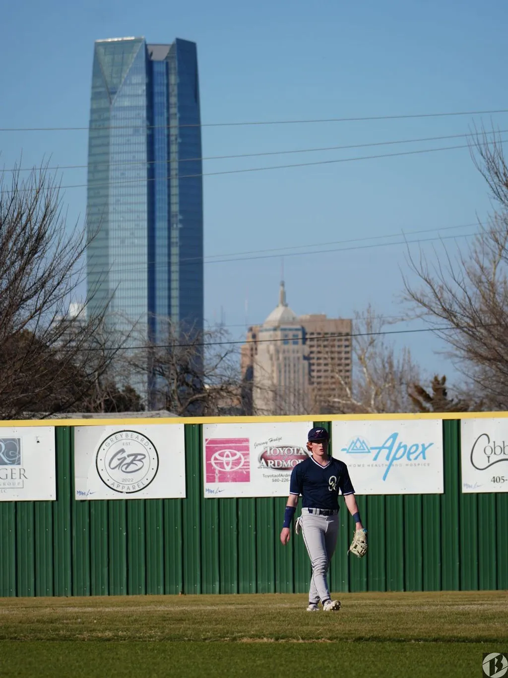 Baseball outfielder in the outfield with the Oklahoma City skyline behind the fence