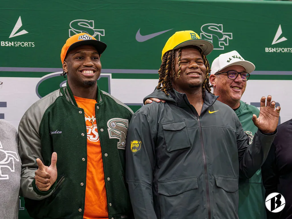 Two athletes in college caps smile beside a coach at their commitment announcement