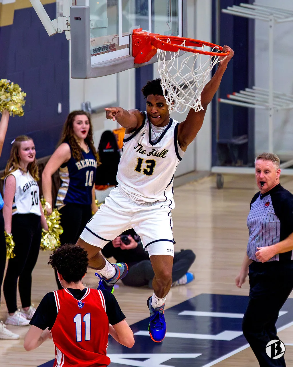Heritage Hall basketball player hangs on the rim after a dunk as cheerleaders and a referee react