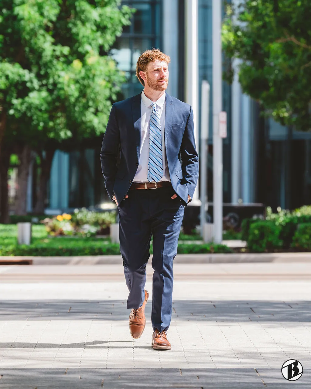 Senior portrait of a young man in a navy suit walking through a plaza