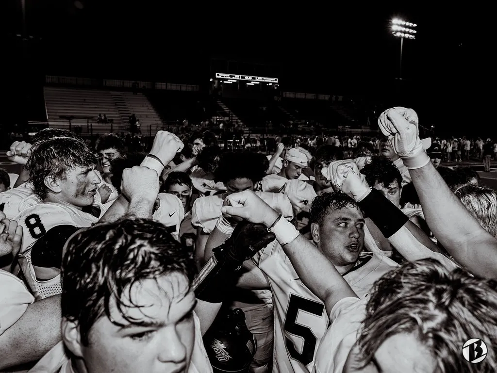 Football players huddle with fists raised under the stadium lights after a night game